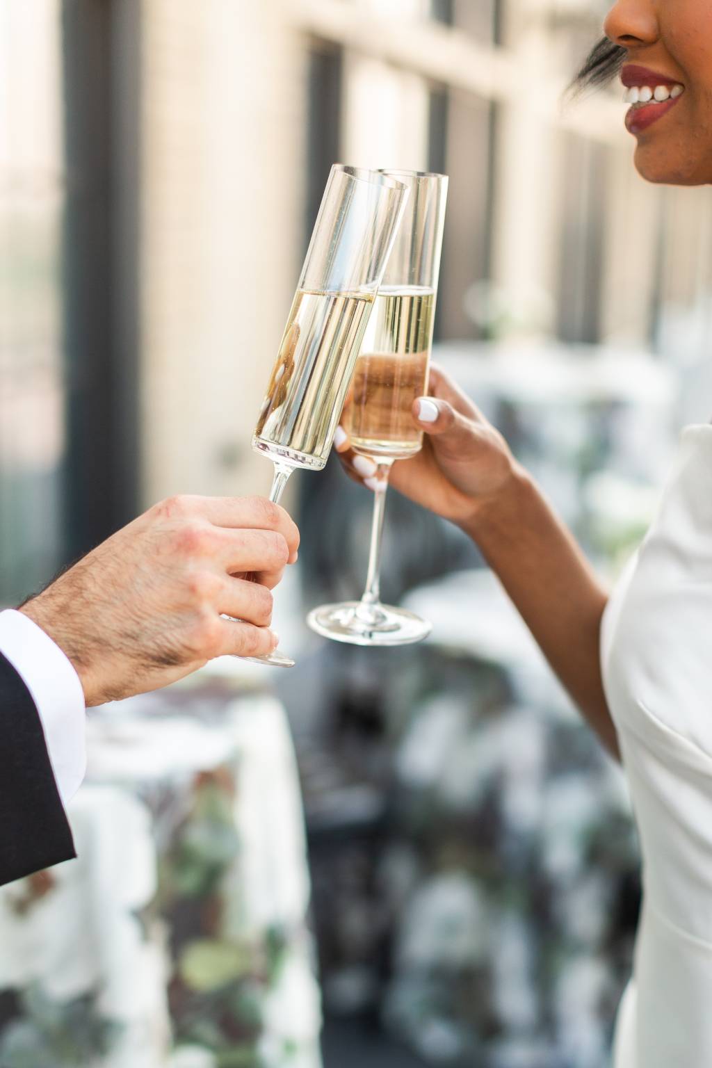 Biracial couple clinks glasses and smiles on rooftop of Chicago wedding venue The Penthouse Hyde Park